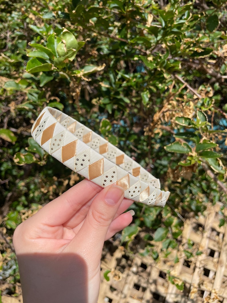 May include: A white headband with a gold and white geometric pattern. The headband is made of a soft, flexible material and is perfect for adding a touch of style to any outfit.