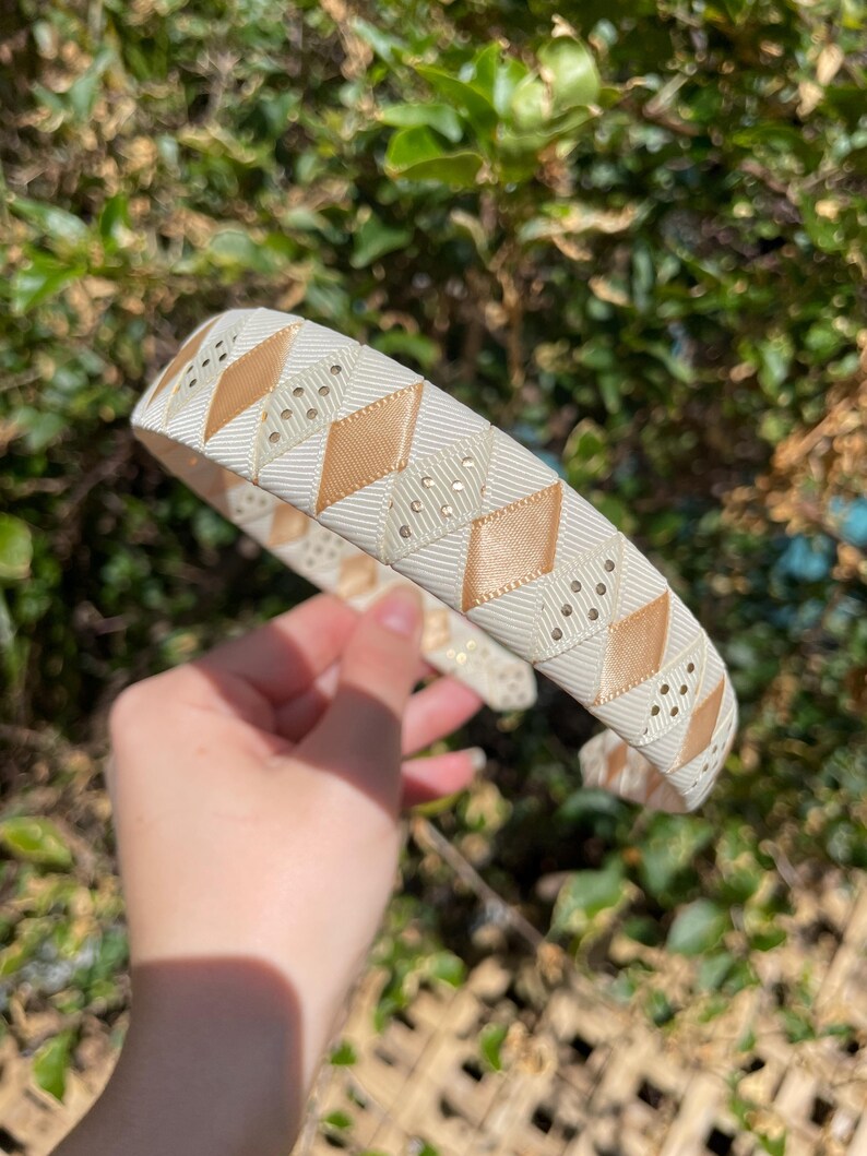 May include: A white and gold headband with a geometric pattern. The headband is made of a soft, flexible material and is perfect for adding a touch of elegance to any outfit.