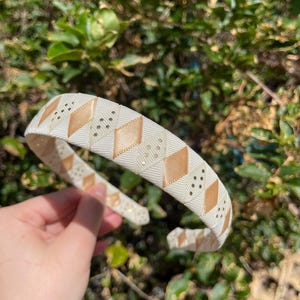May include: A white headband with a gold and white geometric pattern. The headband is made of a soft, flexible material and has a comfortable fit.
