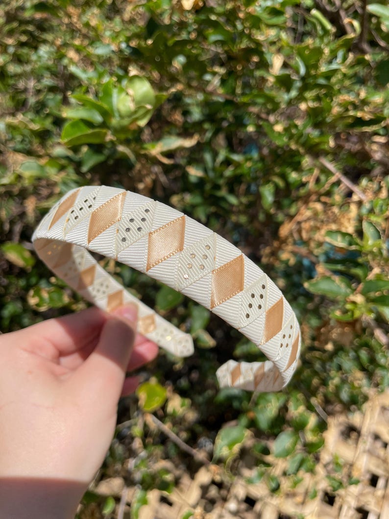May include: A white headband with a gold and white geometric pattern. The headband is made of a soft, flexible material and has a comfortable fit.