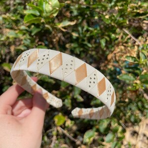May include: A white headband with a gold and white geometric pattern. The headband is made of a soft, flexible material and has a comfortable fit.