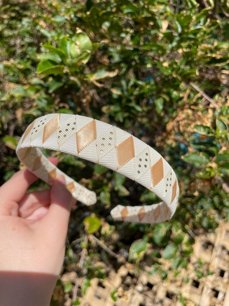 May include: A white headband with a gold and white geometric pattern. The headband is made of a soft, flexible material and has a comfortable fit.