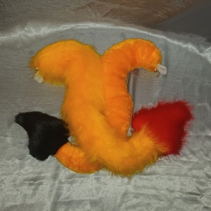 May include: Three fluffy tails in orange, black, and red. The tails are attached to a furry costume piece.