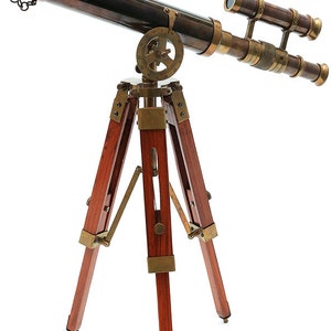 Könnte beinhalten: Ein Messingteleskop mit einem Holzstativ. Das Teleskop hat eine schwarze Oberfläche und eine Messinglinse. Das Stativ ist aus dunklem Holz und hat Messingakzente.