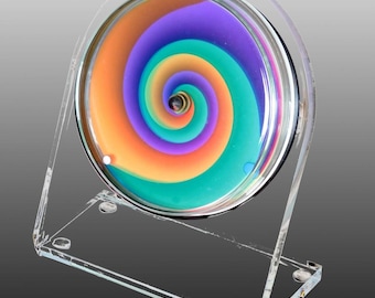Petriplex Vertigo, un orologio da tavolo e da mensola in acrilico realizzato da un artista, con vivaci colori CMYK che mostrano splendide miscele di colori intorno all'orologio.