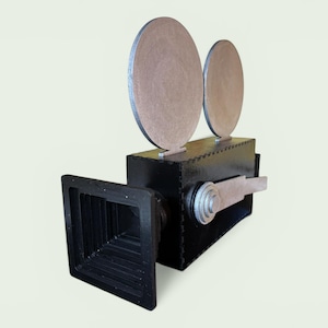 Puede incluir: Una cámara de cine vintage negra con dos elementos circulares plateados en la parte superior. La cámara tiene un cuerpo rectangular y una lente cuadrada en forma de embudo. El asa y otros detalles son plateados.