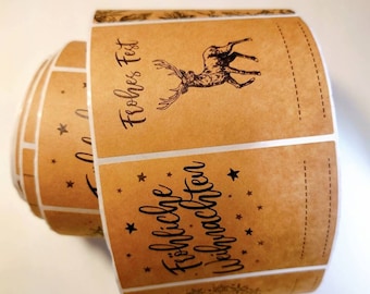 Puede incluir: Rollo de etiquetas de papel marrón con temática navideña. Cada etiqueta presenta una ilustración de ciervo, las palabras "Frohes Fest" y "Fröhliche Weihnachten", y pequeños acentos de estrellas. Las etiquetas tienen una línea punteada para una fácil separación.