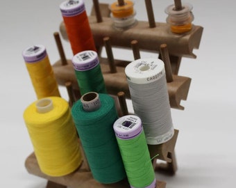 May include: A wooden thread rack with spools of thread in various colours, including yellow, green, orange, and grey. The rack has three tiers and is designed to hold multiple spools of thread.