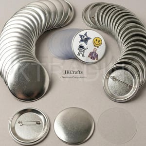 May include: A selection of silver-coloured, round button blanks and clear plastic covers. One button displays a star, a smiley face, an astronaut, and a skeleton. The text "JKCrafts - Premium Components" is visible.
