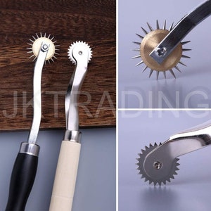 May include: Two silver sewing tools with wooden handles. One tool has a black handle and a circular wheel with sharp points. The other tool has a white handle and a circular wheel with small teeth.