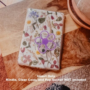 May include: A clear phone case with a floral design featuring pressed flowers and gold accents. A purple pop socket is attached to the back of the case. "Insert Only Kindle, Clear Case, and Pop Socket NOT included" is written below the case.