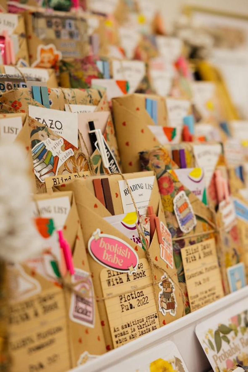 May include: A close-up of a shelf filled with wrapped gifts, each decorated with colorful stickers, twine, and paper. The gifts are labeled with titles like "Blind Date With A Book" and "Reading List".