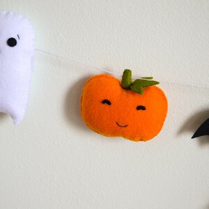 May include: A Halloween garland with a white ghost, an orange pumpkin with a smiling face, and a black bat.