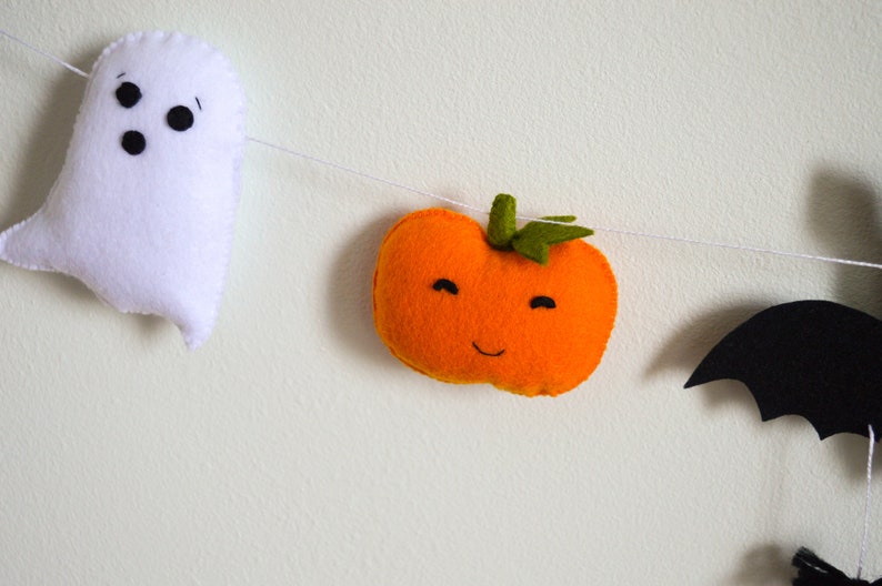 May include: A Halloween garland with a white ghost, an orange pumpkin with a smiling face, and a black bat.
