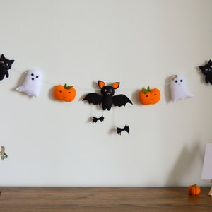 May include: A Halloween garland with black cats, ghosts, bats, and pumpkins. The garland is strung with white thread and has orange felt balls as spacers.