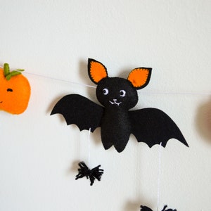 May include: A Halloween garland with a black felt bat with orange ears, two orange felt pumpkins with green stems, and white felt ghosts.