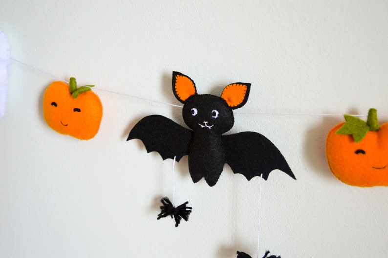 May include: A Halloween garland with a black felt bat with orange ears, two orange felt pumpkins with green stems, and white felt ghosts.