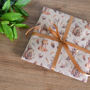 K&ouml;nnte beinhalten: Ein Geschenk, das in braunes Papier mit einem Waldtierdruck eingewickelt ist. Das Papier ist mit Eulen, F&uuml;chsen, Eichh&ouml;rnchen und V&ouml;geln verziert. Das Geschenk ist mit einem braunen Band gebunden.