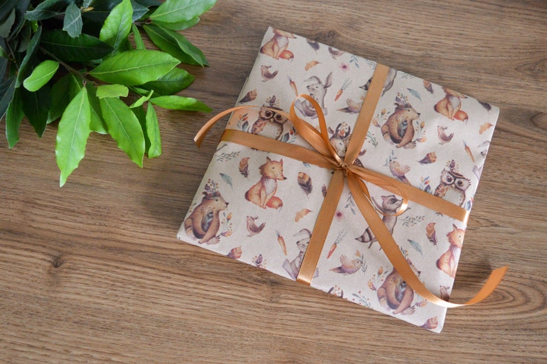 K&ouml;nnte beinhalten: Ein Geschenk, das in braunes Papier mit einem Waldtierdruck eingewickelt ist. Das Papier ist mit Eulen, F&uuml;chsen, Eichh&ouml;rnchen und V&ouml;geln verziert. Das Geschenk ist mit einem braunen Band gebunden.