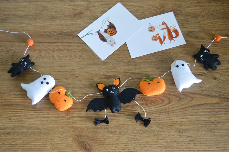 May include: A Halloween garland with black felt bats, ghosts, pumpkins, and cats. The garland is strung with white thread and orange beads.