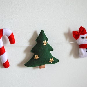 May include: A festive garland with a red and white candy cane, a green felt Christmas tree with gold glitter stars, and a white felt snowman with a red bow and scarf.