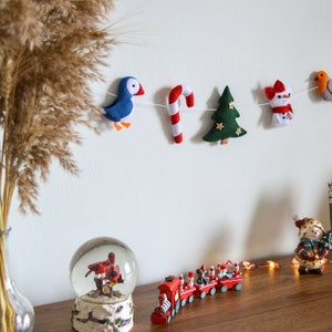 May include: A felt Christmas garland with a blue bird, candy cane, green Christmas tree, snowman, and a robin with holly.