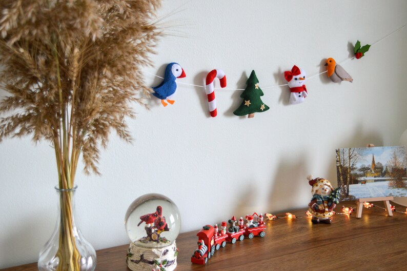 May include: A felt Christmas garland with a blue bird, candy cane, green Christmas tree, snowman, and a robin with holly.