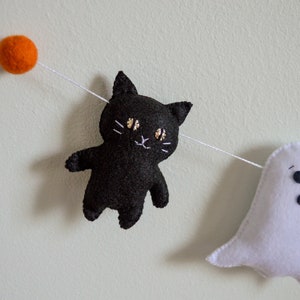 May include: A Halloween garland with a black cat, a white ghost, and orange felt balls.