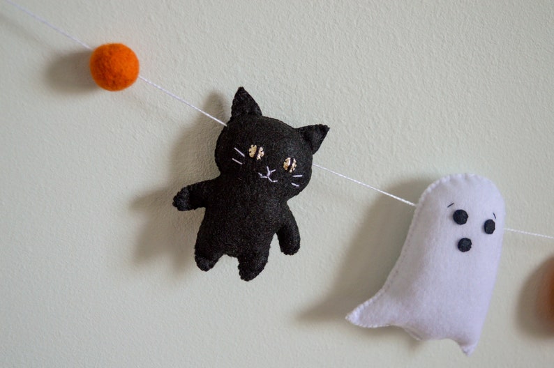 May include: A Halloween garland with a black cat, a white ghost, and orange felt balls.