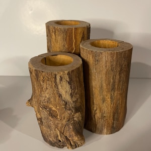 May include: Three wooden candle holders made from tree trunks. The candle holders are different sizes and have a natural wood finish.