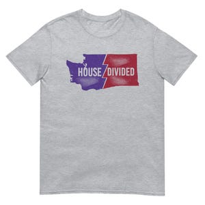 May include: A heather gray t-shirt featuring a graphic of the state of Washington, split into purple and red sections with a lightning bolt. The text "HOUSE DIVIDED" is printed in white.