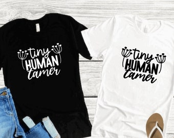 May include: Two t-shirts, one black and one white, with the text "tiny human tamer" printed in white on both shirts.