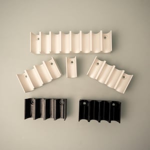 Könnte beinhalten: Fünf weiße Batteriehalter aus Kunststoff und zwei schwarze Batteriehalter aus Kunststoff. Die Halter sind so konzipiert, dass sie mehrere Batterien in einer Reihe aufnehmen können.