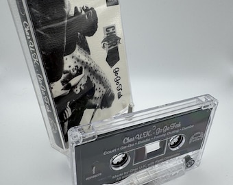 May include: A clear cassette tape labeled "Cher U.K. Go-Go Fish" with a black and white image. The cassette case is transparent, and the tape itself has black text. The text includes song titles and the phrase "Advance Cassette."