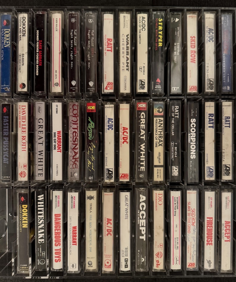 Puede incluir: Una colecci&oacute;n de cintas de casete vintage de varias bandas de rock y heavy metal. Las cintas est&aacute;n en estuches de pl&aacute;stico transparente, con los t&iacute;tulos y nombres de las bandas visibles, incluyendo Dokken, AC/DC y Warrant. Las cintas est&aacute;n dispuestas en una cuadr&iacute;cula.