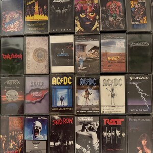 Puede incluir: Una colecci&oacute;n de cintas de casete vintage con varias bandas de rock y metal. Se ven t&iacute;tulos de &aacute;lbumes y nombres de bandas, como AC/DC y Skid Row. Las cintas est&aacute;n en estuches de pl&aacute;stico transparente.