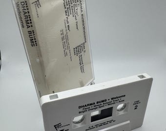 May include: A white Dharma Bums "Welcome" cassette tape with the tracklist visible. The cassette case is open, revealing the tape's label and the album title. The cassette tape is a vintage music collectible.