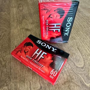 May include: Two Sony HF High Fidelity audio cassette tapes in their original plastic shrink wrap. The packaging features a red and black color scheme with the text Sony, HF, High Fidelity, Normal Bias, and 60 min printed on the front covers.