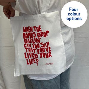 May include: White tote bag with red text saying "WHEN THE BOMBS DROP DARLIN' CAN YOU SAY THAT YOU'VE LIVED YOUR LIFE?" with "SAM FENDER HYPERSONIC MISSILES" below. A circle with "Four colour options" is in the upper right.