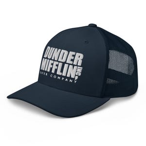 Può includere: Un cappellino trucker blu navy con retro in rete e pannello frontale strutturato. La parte anteriore presenta un testo ricamato in bianco che recita DUNDER MIFFLIN INC. PAPER COMPANY in un carattere impilato, nitido e professionale.