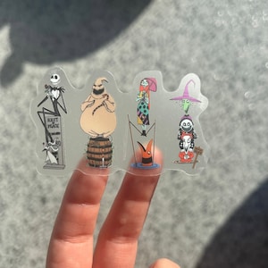 May include: Five clear stickers featuring characters from the Nightmare Before Christmas. The stickers feature Jack Skellington, Sally, Oogie Boogie, the Mayor, and Lock, Shock, and Barrel. The stickers are on a white background.