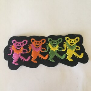 May include: Four colorful dancing bears embroidered on a black patch. The bears are pink, orange, green, and yellow.