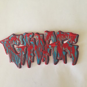 May include: Red and blue embroidered patch with the word "GWAR" in a dripping, stylized font.