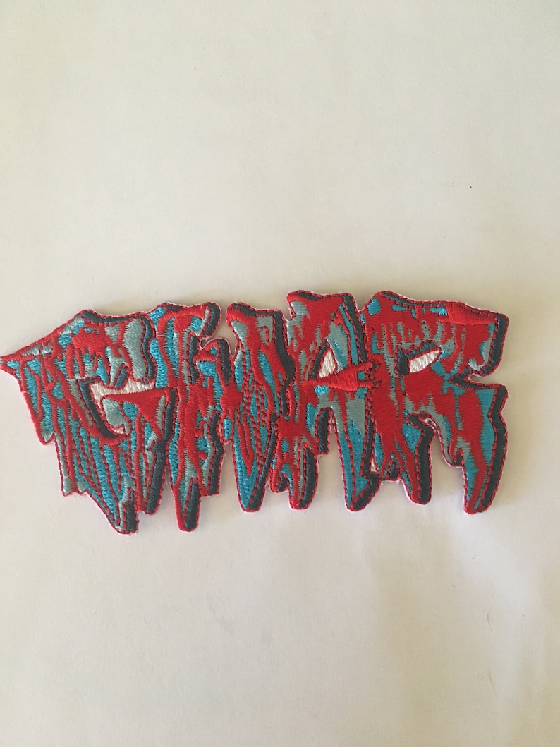 May include: Red and blue embroidered patch with the word "GWAR" in a dripping, stylized font.