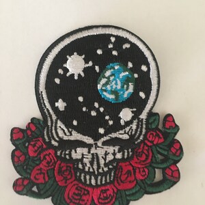 May include: Embroidered patch featuring a black and white skull with a white outline, a black background with a white sun, moon, and blue earth, and a red rose garland.