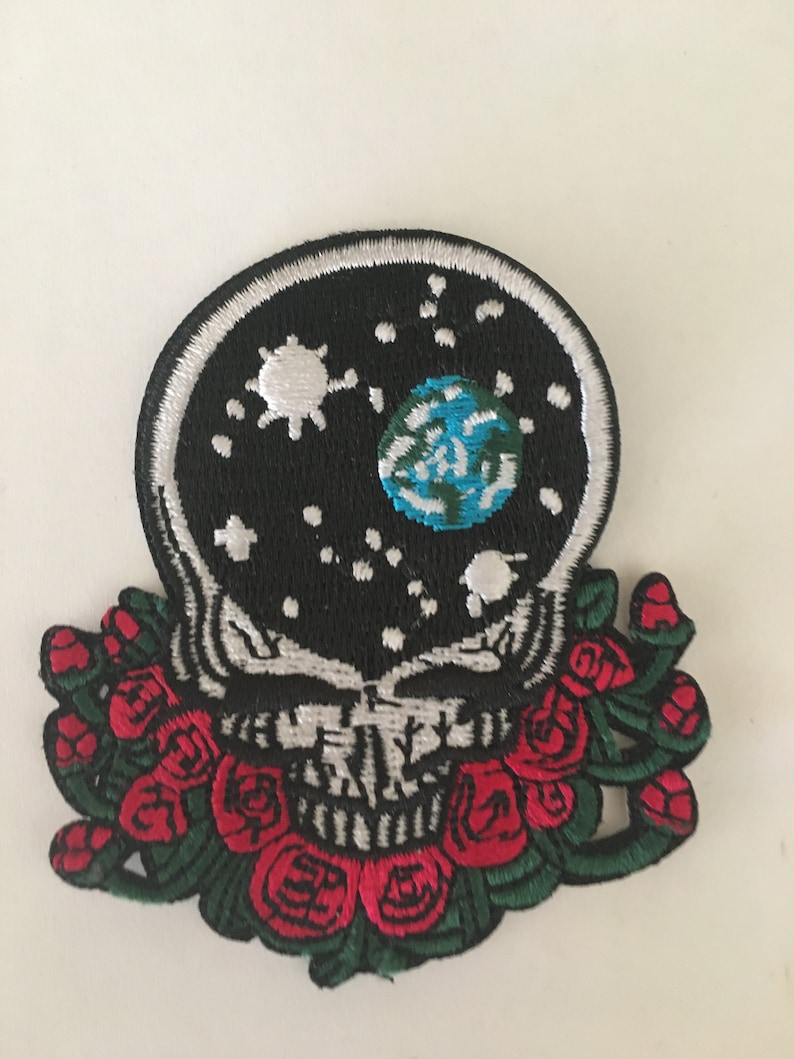 May include: Embroidered patch featuring a black and white skull with a white outline, a black background with a white sun, moon, and blue earth, and a red rose garland.