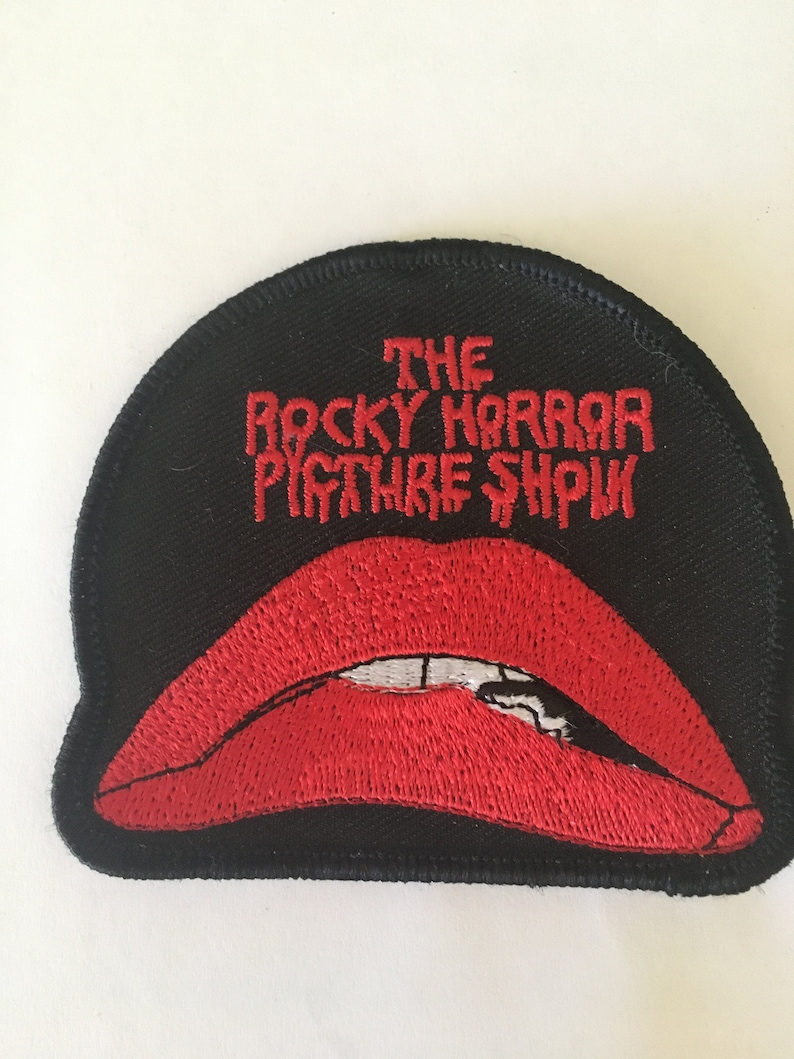 May include: Black embroidered patch with a red, open-mouthed lip design. The text "THE ROCKY HORROR PICTURE SHOW" is embroidered in red on the patch.