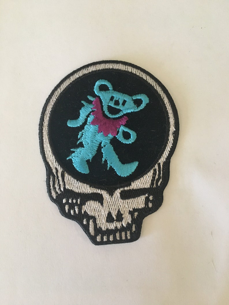 May include: A blue and purple embroidered patch of a dancing bear inside a black and white skull graphic.