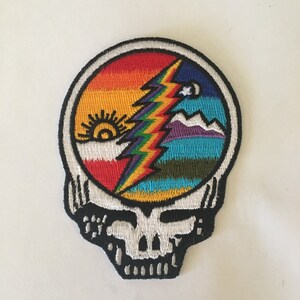 May include: A colorful embroidered patch featuring the Grateful Dead's iconic Steal Your Face logo with a rainbow lightning bolt and a sun and moon design.