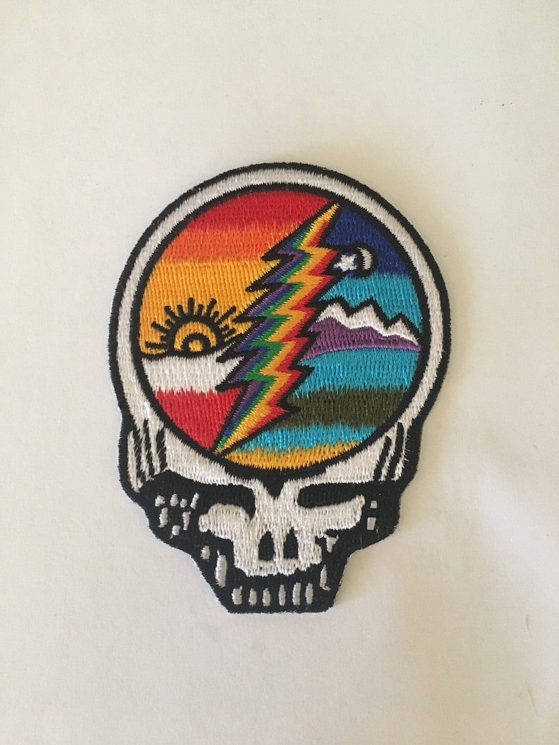 May include: A colorful embroidered patch featuring the Grateful Dead's iconic Steal Your Face logo with a rainbow lightning bolt and a sun and moon design.
